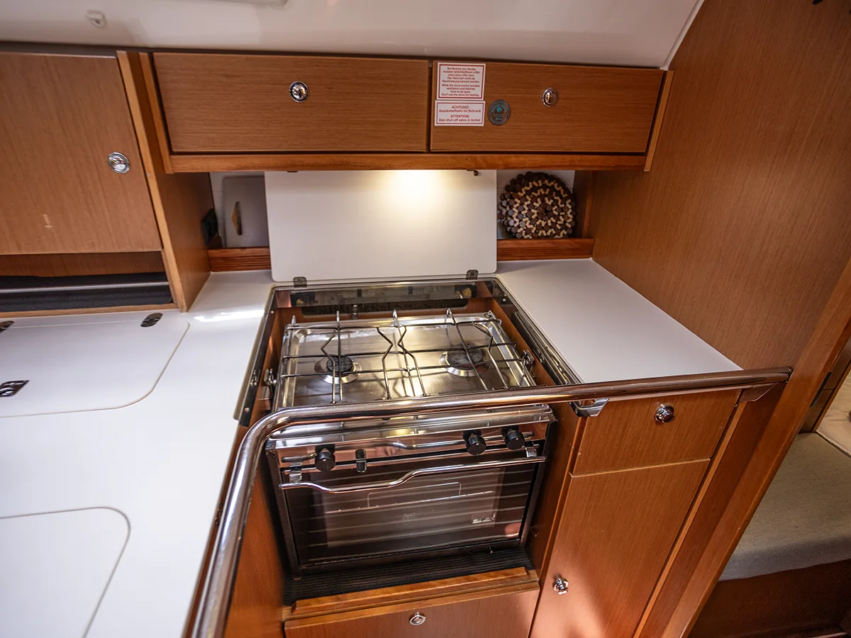 Interior view of a Bavaria 36 boat kitchen featuring a stainless steel stove and oven, surrounded by wooden cabinets and a white countertop.