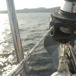 An outboard motor mounted on the back of a boat, overlooking a sunlit lake with distant hills, viewed from the yachtmaster theory course boat's stern.