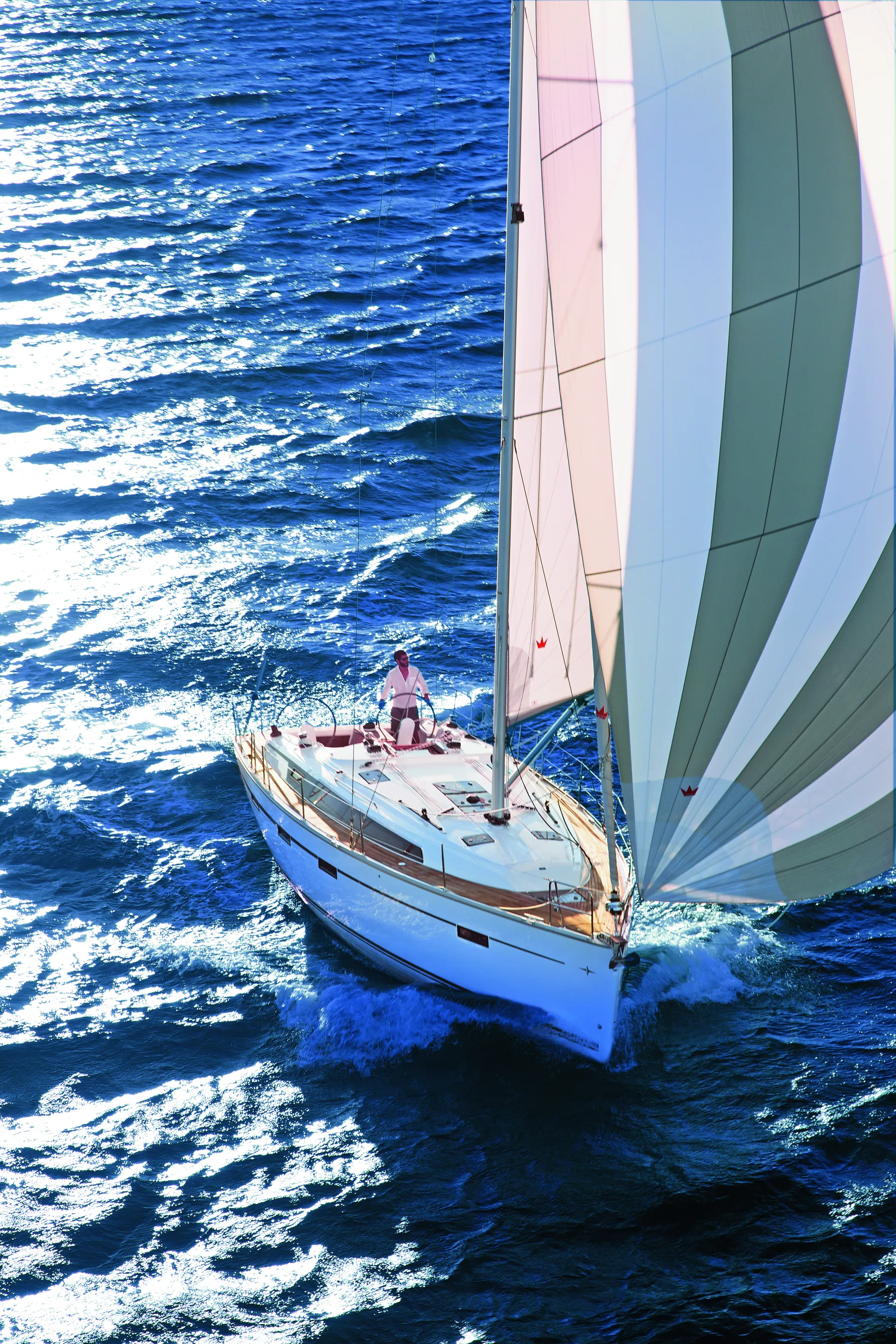 A white Bavaria 46 Style sailing boat with striped sails moves through blue, sunlit water. One person is visible on deck, steering, while sunlight reflects off the waves.
