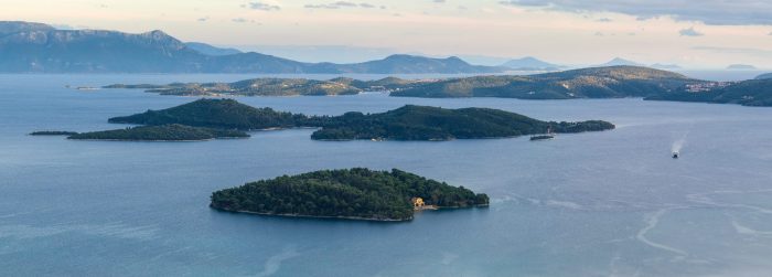 Plan a holiday to enjoy the panoramic view of a serene lake with scattered green islands and a few boats cruising the waters, under a vast, cloudy sky.