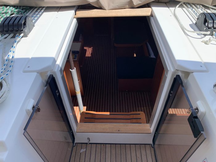 View from the deck of a Bavaria C42 looking into the cabin entrance, featuring wooden steps and floors with white trim and accents, under bright daylight.