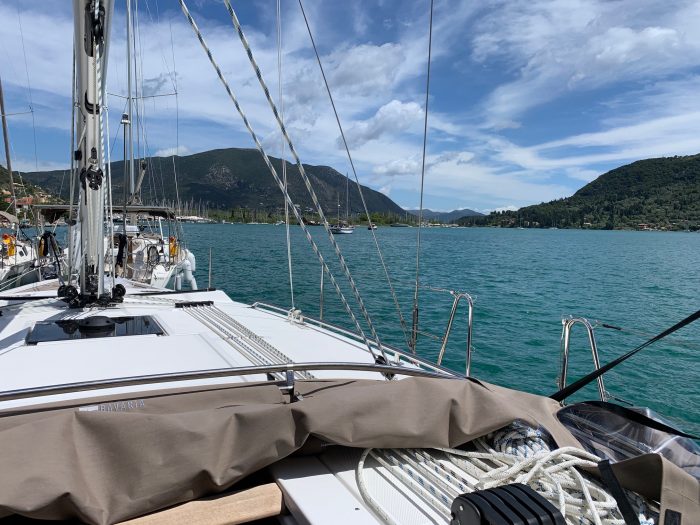 View from the deck of a Bavaria C42 sailboat showing ropes, a calm blue lake, green hills in the background, and clear skies.