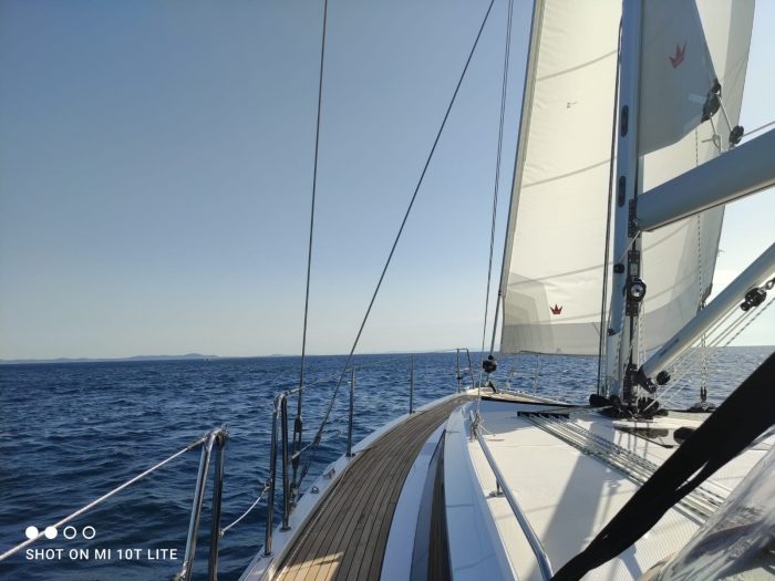 View from the deck of a sailboat with full sails set, sailing on calm blue waters under a clear sky near Vliho.