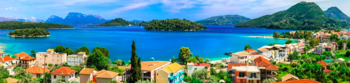 Panoramic view of a coastal town with colorful buildings, lush green islands in the distance, and a vibrant blue sea under a clear sky showcasing amazing June offers.