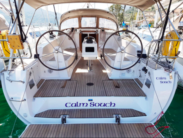 Rear view of a yacht named "Calm Souch" with dual steering wheels, a wooden deck, and a covered seating area, docked in a marina practicing green yachting in