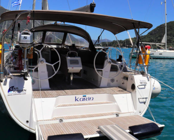 Close-up view of the stern of a modern white sailing yacht named "Karin," showcasing dual steering wheels, a wooden deck, and seating, moored in a sunny marina promoting green yach