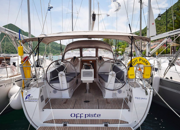 Rear view of a luxurious green yachting vessel named "off piste" docked at a marina, surrounded by other boats, with mountains in the background.