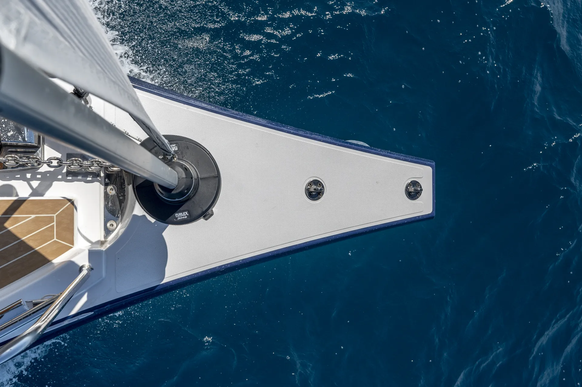 Aerial view of a Bavaria C46 sailboat’s bow cutting through deep blue water, with visible deck details and waves along the boat’s side.